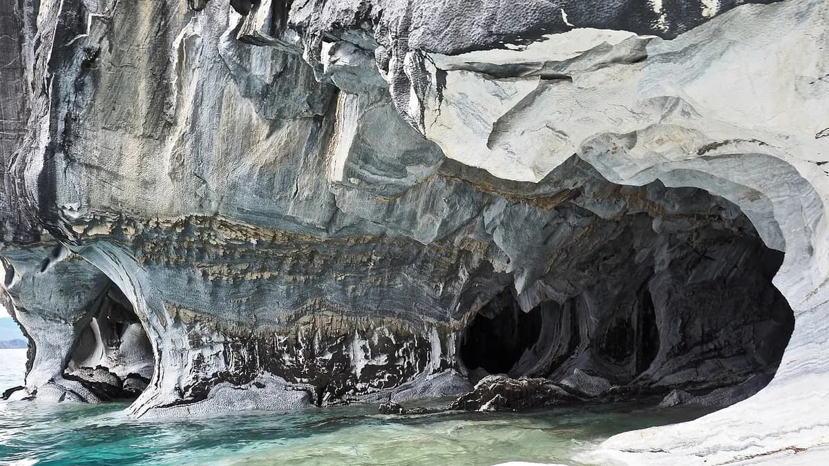 Interior de una caverna con vetas blancas y grises reflejadas en agua turquesa
